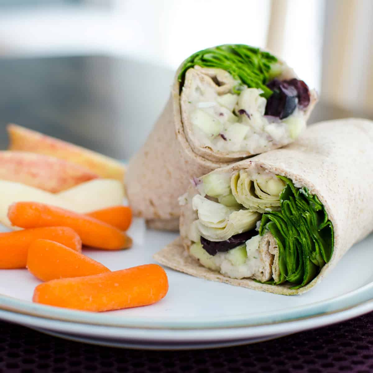vegan Greek sandwich wrap cut in half on a plate with carrots and sliced apple