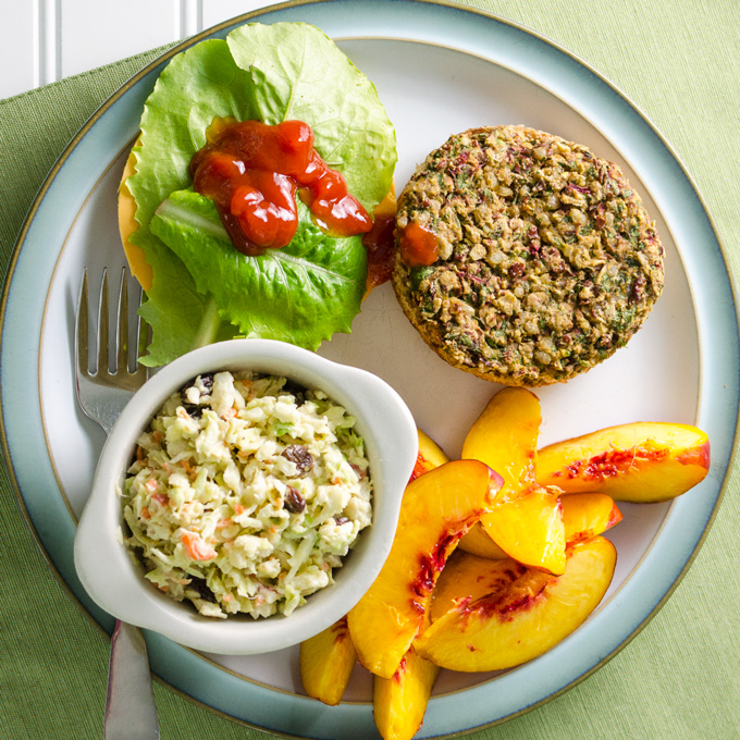 veggie coleslaw on a plate with a kale veggie patty and sliced peaches